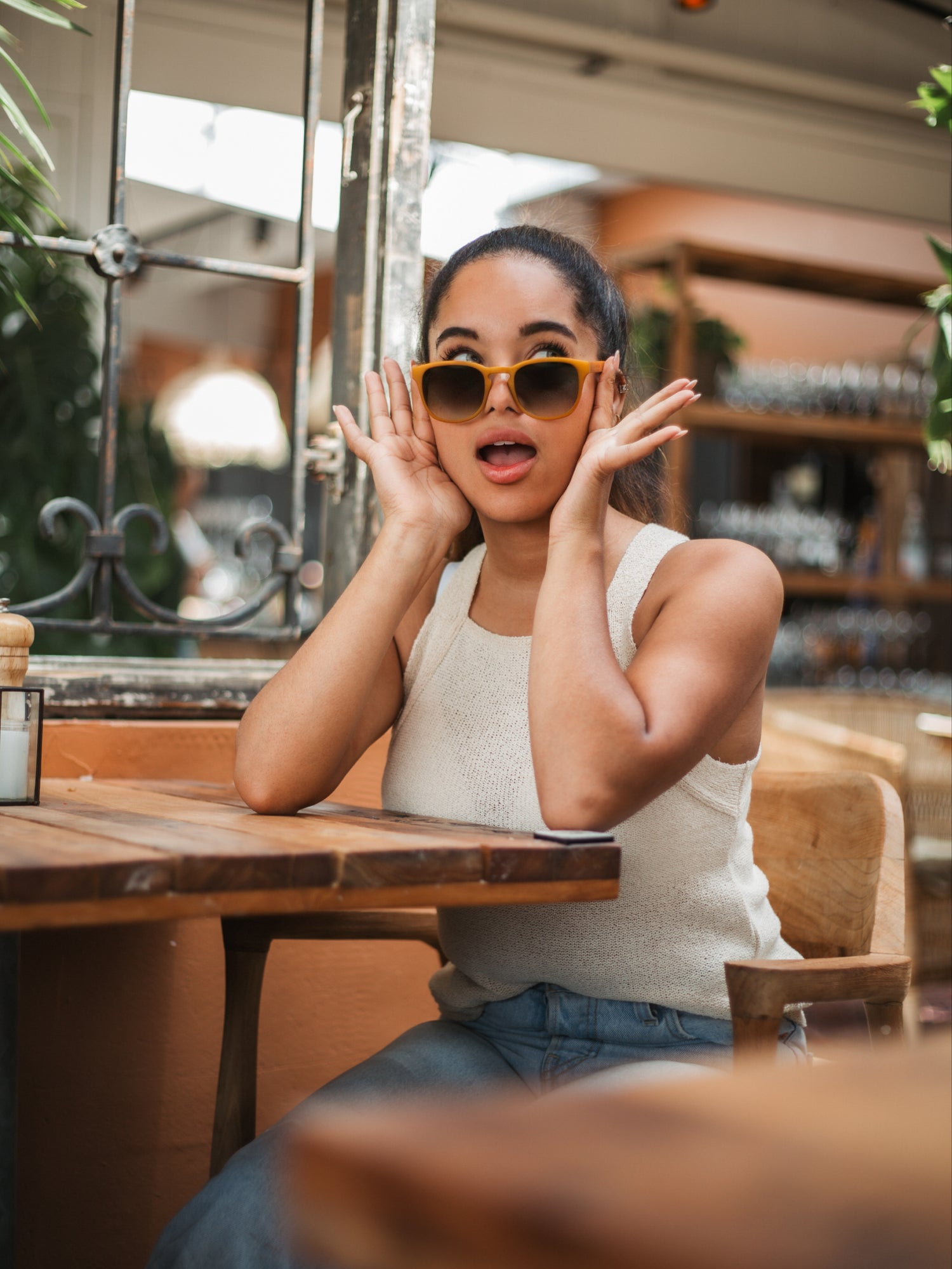 Vrouw in een restaurant met een duurzame 3D-geprinte zonnebril lachend en kijkend omhoog